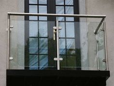 a balcony with glass doors and railings on the side of a gray building in front of a black door