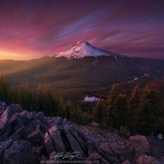 the sun is setting over a mountain with rocks and pine trees in front of it