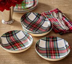 three plaid plates and two silverware on a table with red flowers in a vase