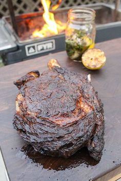 a steak is sitting on a cutting board next to some lemons and a fire