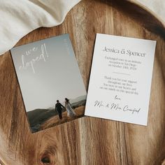 two wedding cards sitting on top of a wooden table