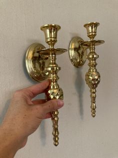 a hand is holding two golden candlesticks on the wall next to each other