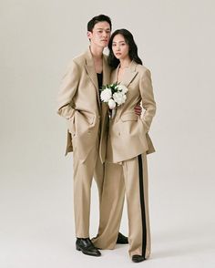 a man and woman standing next to each other wearing suits with flowers in their lapels