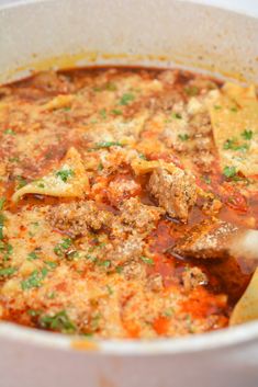 a white bowl filled with meat and vegetable soup next to tortilla chips on the side