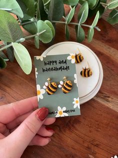 a pair of bee earrings on top of a card next to a potted plant