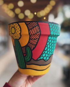 a hand holding up a colorful cup with a cactus painted on the outside and inside