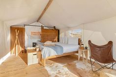 a bed sitting inside of a white tent next to a wooden table and chair on top of a hard wood floor