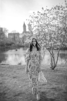 black and white photo of woman in floral dress walking by tree with flowers on it