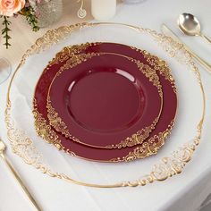 a red plate with gold trim sits on a white table cloth next to silverware