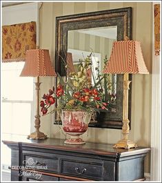 a vase with flowers on top of a table next to two lamps and a mirror