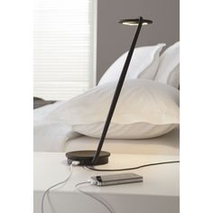 a lamp that is sitting on top of a white table next to a bed with pillows