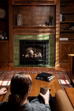 a person sitting on a couch in front of a fireplace with a book and cup