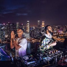 two men standing next to each other in front of a cityscape at night