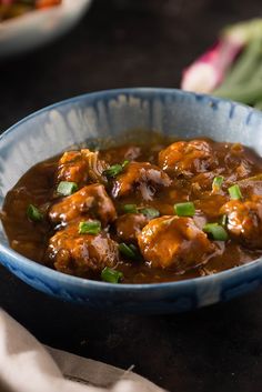 a blue bowl filled with meat covered in gravy and garnished with green onions