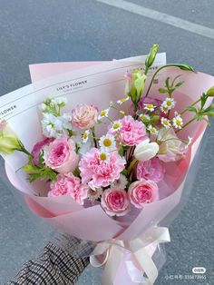 a bouquet of pink and white flowers is held by someone's hand on the street