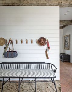 a bench sitting in front of a wall with hats hanging on it's hooks