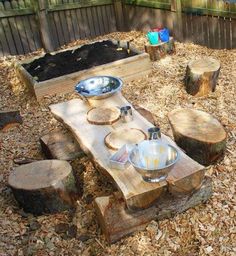 an outdoor table made out of wood and metal bowl on it's end, surrounded by logs