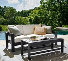 a couch sitting on top of a wooden table next to a swimming pool with trees in the background