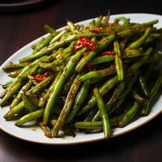 a white plate topped with green beans covered in seasoning on top of a wooden table