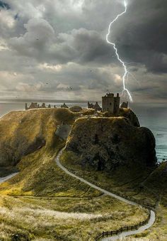 a lightning bolt strikes over a castle on top of a hill next to the ocean