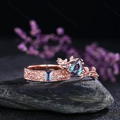 two wedding rings with blue topazte and diamonds on a rock next to purple flowers