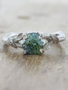 a green ring with leaves on the sides and a stone in the middle, sitting on top of a piece of wood