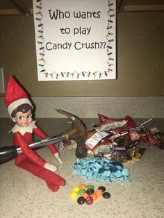 an elf is playing with candy in front of a sign that says who wants to play candy crush?