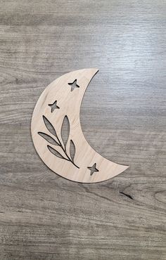 a wooden moon with leaves and stars on it, sitting on a wood surface in the shape of a crescent