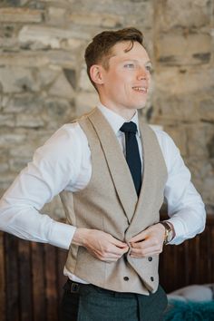 a man wearing a vest and tie standing in front of a stone wall with his hands on his hips