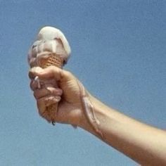 a hand holding an ice cream cone in front of a blue sky with white clouds