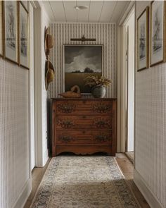 an old dresser is in the hallway between two paintings on the wall and a rug