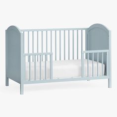 a baby crib with a white sheet on the bottom half and a light blue headboard