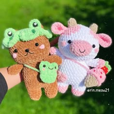 a hand holding three small stuffed animals in it's left hand, with grass in the background