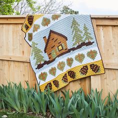 a crocheted blanket hanging on the side of a fence next to green plants