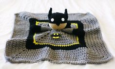 a crocheted batman blanket on top of a white bed with a stuffed animal