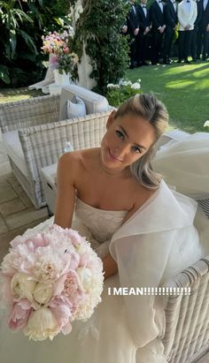 a woman in a wedding dress sitting on a wicker chair holding a pink and white bouquet