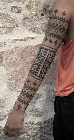 a man with a tattoo on his arm is standing in front of a stone wall