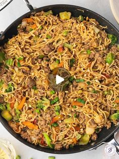 a skillet filled with noodles and vegetables on top of a white table next to utensils