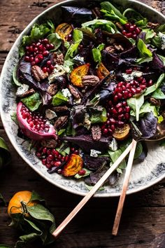 a salad with beets, spinach and other vegetables on a plate next to two wooden spoons