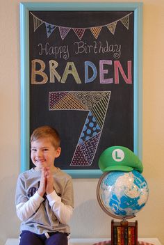 a young boy sitting in front of a birthday sign