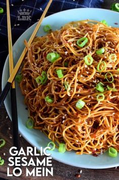 a white plate topped with noodles covered in sesame seeds and green onions next to chopsticks