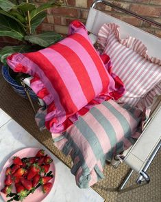 a pink and grey striped pillow sitting on top of a chair next to a bowl of strawberries