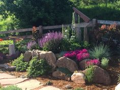 a garden with rocks and flowers near a wooden fence