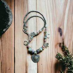 Introducing our Handmade Earth and Moon Necklace - a stunning piece that celebrates the beauty and mystique of our natural world. Expertly crafted with care and attention to detail, this necklace captures the essence of earthy elegance and cosmic beauty. The earth-toned beads of the necklace evoke a sense of balance and connection to the natural world, while the authentic figures and moon charm add a touch of celestial magic. Every bead is carefully chosen to complement the others, creating a harmonious design that reflects the beauty of the universe. Handmade with love and care, this necklace is a unique and one-of-a-kind piece that embodies the artisanal spirit. The authentic figures are each individually crafted to represent the diversity and richness of cultures and traditions across t Nature-inspired Healing Necklace With Round Pendant, Bohemian Beaded Necklaces With Round Pendant, Handmade Unique Moon Necklace, Bohemian Jewelry With Moon Charm And Round Beads, Bohemian Moon Phase Round Beaded Jewelry, Unique Handmade Moon Shaped Necklace, Handmade Moon Shaped Necklace, Artisan Moon Charm Necklaces, Bohemian Beaded Necklace With Round Pendant