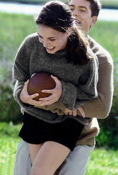 a man carrying a woman on his back while holding a football in their hands and laughing