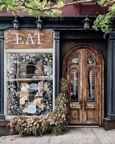 a store front with flowers in the foreground and an open door on the other side