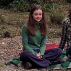 two young women sitting on a blanket in the woods, one is smiling at the camera