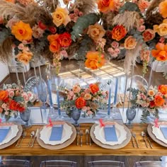 the table is set with orange flowers and blue place settings for an elegant dinner party