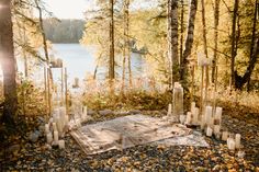 candles are arranged on a blanket in the woods near a body of water and trees