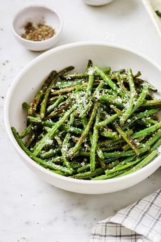 a white bowl filled with green beans covered in parmesan sprinkles